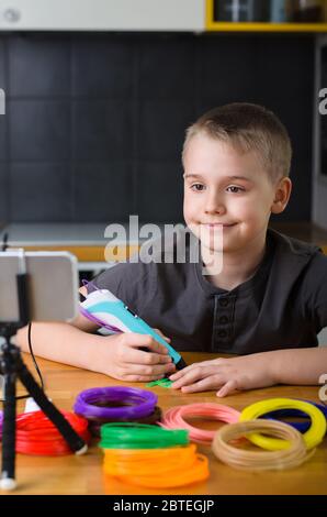 Child creating with 3d printing pen. Happy boy does something with colored ABS plastic and using online lesson. Creative hobby at home, technology, le Stock Photo