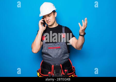 Young workman with helmet making phone call and speaking on blue background Stock Photo