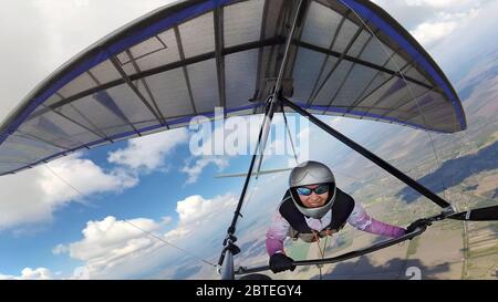 Happy smiling woman hang glider pilot high in the sky with cumulus clouds. Selfie by action camera Stock Photo
