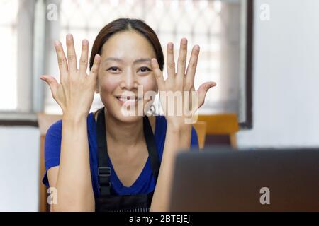 Portrait of happy asian woman working from home with hand up. Stock Photo