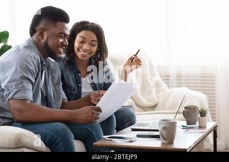 Young african american spouses checking documentation at home, reading insurance agreement Stock Photo