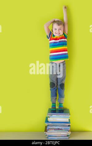 A joyful smiling child is standing on a stacked of children's books. Green background. Stock Photo