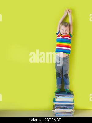 A joyful smiling child is standing on a stacked of children's books. Green background. Stock Photo