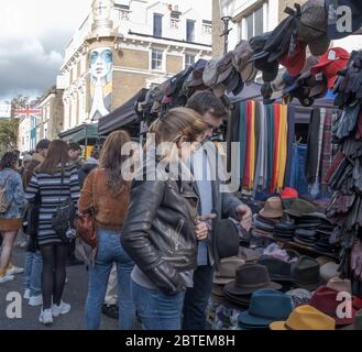 A couple shops for hats at Portobello Road Street Market. Crowded stalls in background. Notting Hill, West London, England, UK. Stock Photo