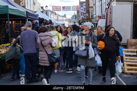 Crowds of tourists & Londoners shopping at Portobello Road Market. Street banner overhead with two British Flags. Notting Hill, West London, England Stock Photo