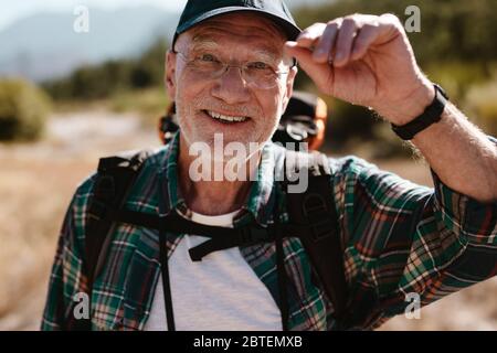Happy senior man on hiking trip looking at camera and smiling. Fit elderly man enjoying on a hiking trip. Stock Photo