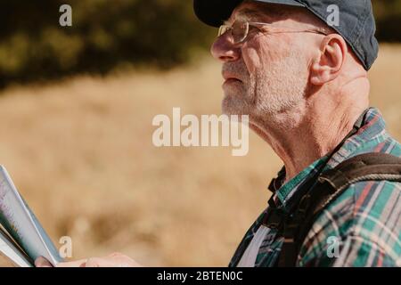 Senior man with a map looking for the directions. Fit old man on a hiking trip using map to find directions. Stock Photo