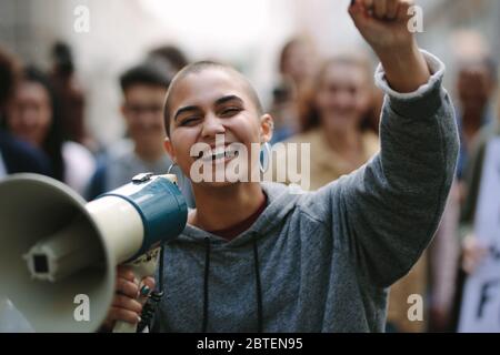 Smiling woman protesting with a bullhorn on the street with people in background. Female with a megaphone as she participates in a street demonstratio Stock Photo