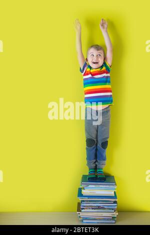 A joyful smiling child is standing on a stacked of children's books. Green background. Stock Photo