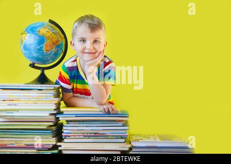 The boy sits next to the children's books and the globe. Green background. Stock Photo