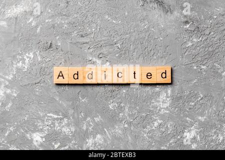 Addicted word written on wood block. Addicted text on cement table for your desing, Top view concept. Stock Photo