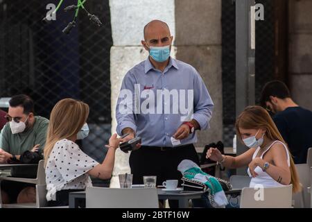 Madrid, Spain. 25th May, 2020. Customers wearing protective face masks in an outdoor terrace table of a cafe in Plaza Mayor paying with a phone. Madrid has entered the so-called Phase One transition from the coronavirus lockdown, allowing many shops to reopen as well as restaurants to serve customers outdoors. Credit: Marcos del Mazo/Alamy Live News Stock Photo