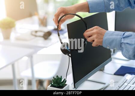 Contact center worker placing his headset on computer monitor at office, closeup of hands. Copy space Stock Photo