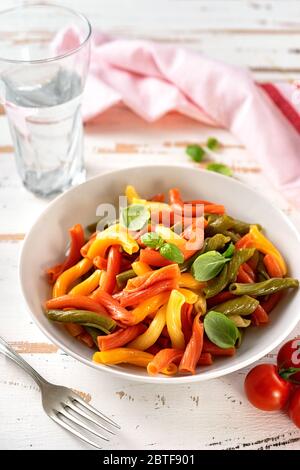 Delicious and colorful penne in a white plate on wooden background
