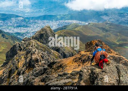 Mountain climber with ropes and walking sticks enjoying the view, making a phone call after reaching the Rucu Pichincha Volcano Peak, Quito, Ecuador. Stock Photo