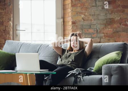 Shocked, scared. Young woman working or studying at home with laptop on sofa, concentrated. Copyspace for your ad. Finance, business, work, gadgets and tech concept. Freelance, education, remote work. Stock Photo