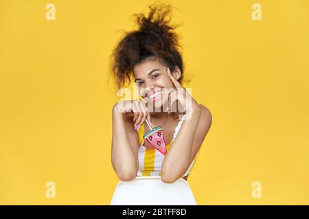 Happy african teen girl hold candy sit on chair on yellow background, portrait. Stock Photo