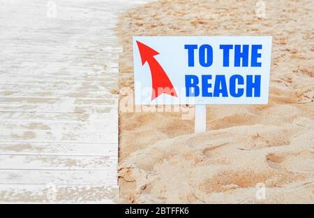 Sign with a sign to the beach on the background of sand and a boardwalk. Stock Photo