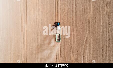 Aerial view of a blue tractor working in a field with a fertilizer and seed spreader Stock Photo