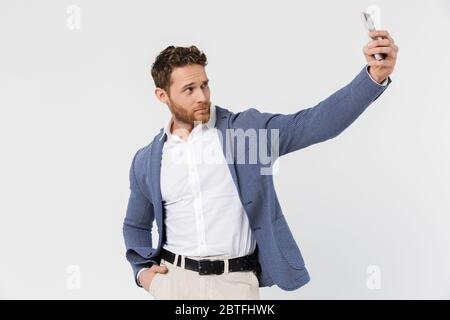 Image of confident handsome man in jacket taking selfie photo on smartphone isolated over white background Stock Photo