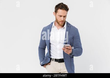 Image of confident serious man wearing jacket typing on smartphone isolated over white background Stock Photo