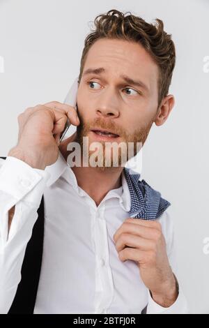 Image of confused blonde man holding jacket and talking on cellphone isolated over white background Stock Photo