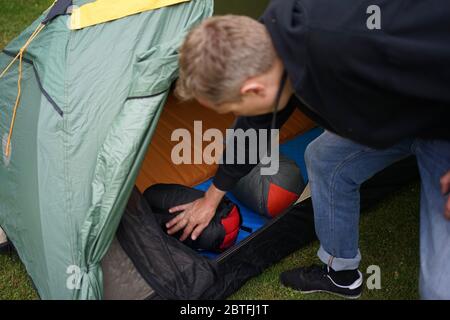 Close up of a man setting up a tent for camping, putting sleeping bags and self inflatable air mats inside the tent. Stock Photo