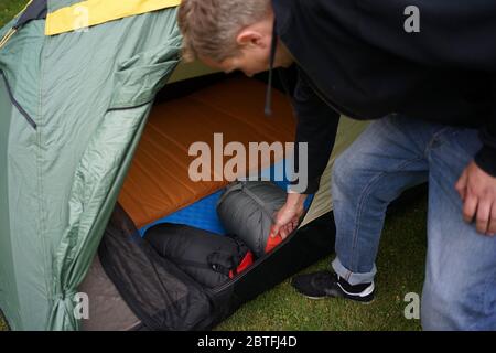 Close up of a man setting up a tent for camping, putting sleeping bags and self inflatable air mats inside the tent. Stock Photo