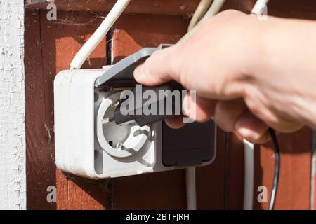 Closeup of a hand inserting a plug into a socket mounted outdoor, shallow dof Stock Photo
