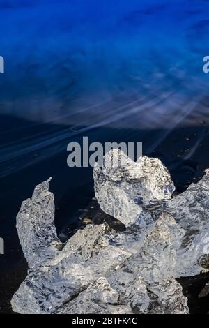 Melting chunk of clear glacial ice, originally calved into Jökulsárlón Lagoon from the Breiðamerkurjökull Glacier, at Diamond Beach on the South Coast Stock Photo