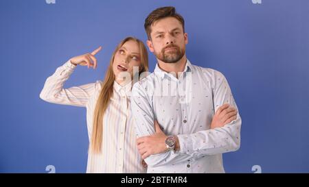 Young couple isolated on the blue background. Woman gesticulation showing the boyfriend, husband is crazy. Stock Photo