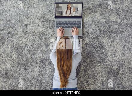 Doctor and patient online. Girl has video tutorial web call using laptop lying on gray floor at home. Stock Photo