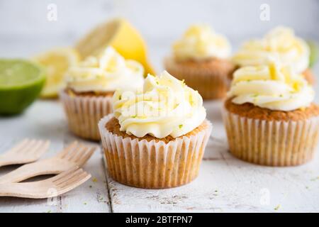 Lemon and poppy seed cupcakes with cheese cream frosting and lemon and lime zest on a rustic white wooden table Stock Photo