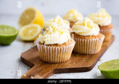 Lemon and poppy seed cupcakes with cheese cream frosting and lemon and lime zest on a cutting board Stock Photo