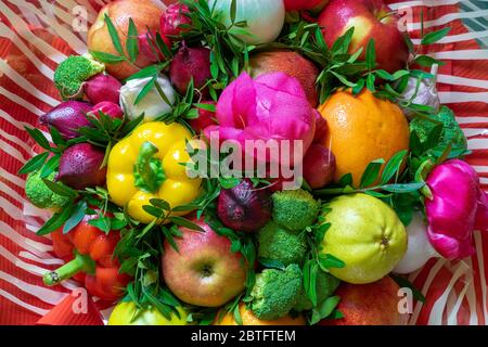 A wonderful multicolored arrangement of a variety fresh fruits and vegetables, pink peonies and green leaves on a red-white striped background Stock Photo