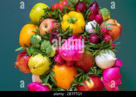An amazing colorful composition of a variety fresh fruits and vegetables, pink peonies and green leaves on a green background Stock Photo