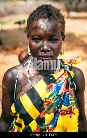 BOYA TRIBE, SOUTH SUDAN - MARCH 10, 2020: Woman in traditional colorful clothes and accessories with ritual piercing and scar modifications looking at Stock Photo