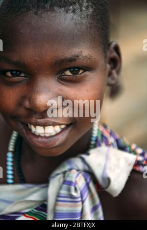 TOPOSA TRIBE, SOUTH SUDAN - MARCH 12, 2020: Girl in colorful garment with beads smiling and looking at camera in village of Toposa Tribe in South Stock Photo