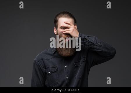 Young man with hand on face covering eyes for surprise standing over isolated gray background . Stock Photo