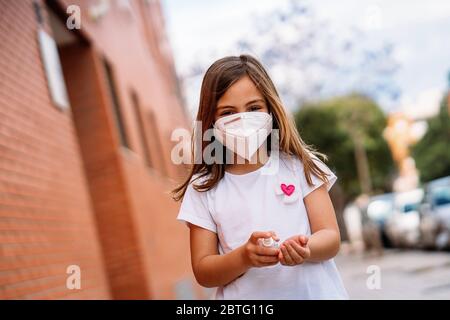 Little girl wearing mask disinfecting her hands with hydroalcoholic gel. Stock Photo
