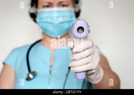 Coronavirus symptoms, woman in medical mask measures body temperature. Doctor looks at digital isometric non-contact thermometer in her hands Stock Photo