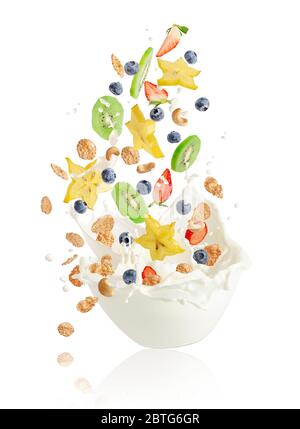 Fresh fruits, berries, corn flakes and nuts falling into the bowl with splashing milk. Healthy muesli breakfast concept. Stock Photo