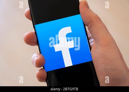 A man's hand holding a smartphone displaying a large logo for the social media app Facebook Stock Photo