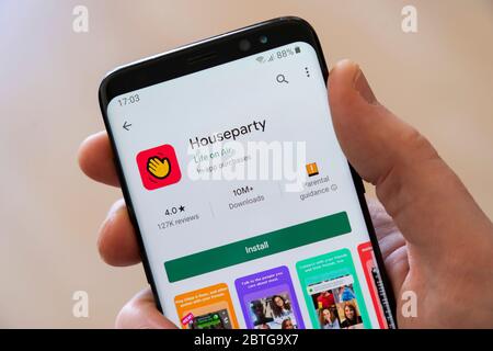 A man's hand holding a smartphone displaying the Google Play install screen for the video calling app Houseparty Stock Photo
