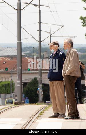 Belgrade, Serbia - May 21, 2020: Two senior men wearing face surgical masks standing at zebra crossing next to a tram road Stock Photo