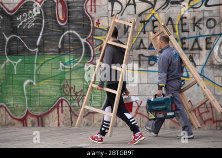 Belgrade, Serbia - May 21, 2020: Two workers carrying wooden ladders and tool boxes while walking city street sidewalk Stock Photo