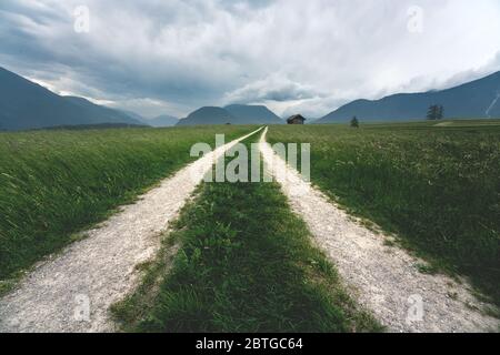 Dirt road through windy stormy grass landscape with hut in the Austrian Alps, Mieminger Plateau, Tyrol, Austria Stock Photo