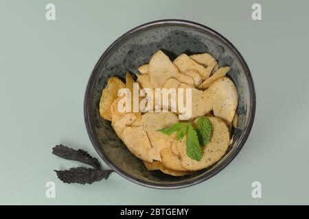 Lamb and mint potato crisps in bowl with fresh mint leaves on light green background Stock Photo