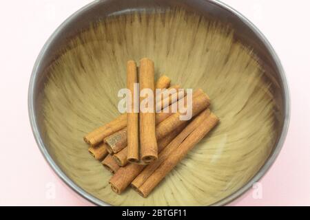 Closeup of cinnamon spice sticks in brown bowl on pink background Stock Photo