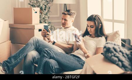 young couple with smartphones sitting on the sofa in a new apartment . Stock Photo